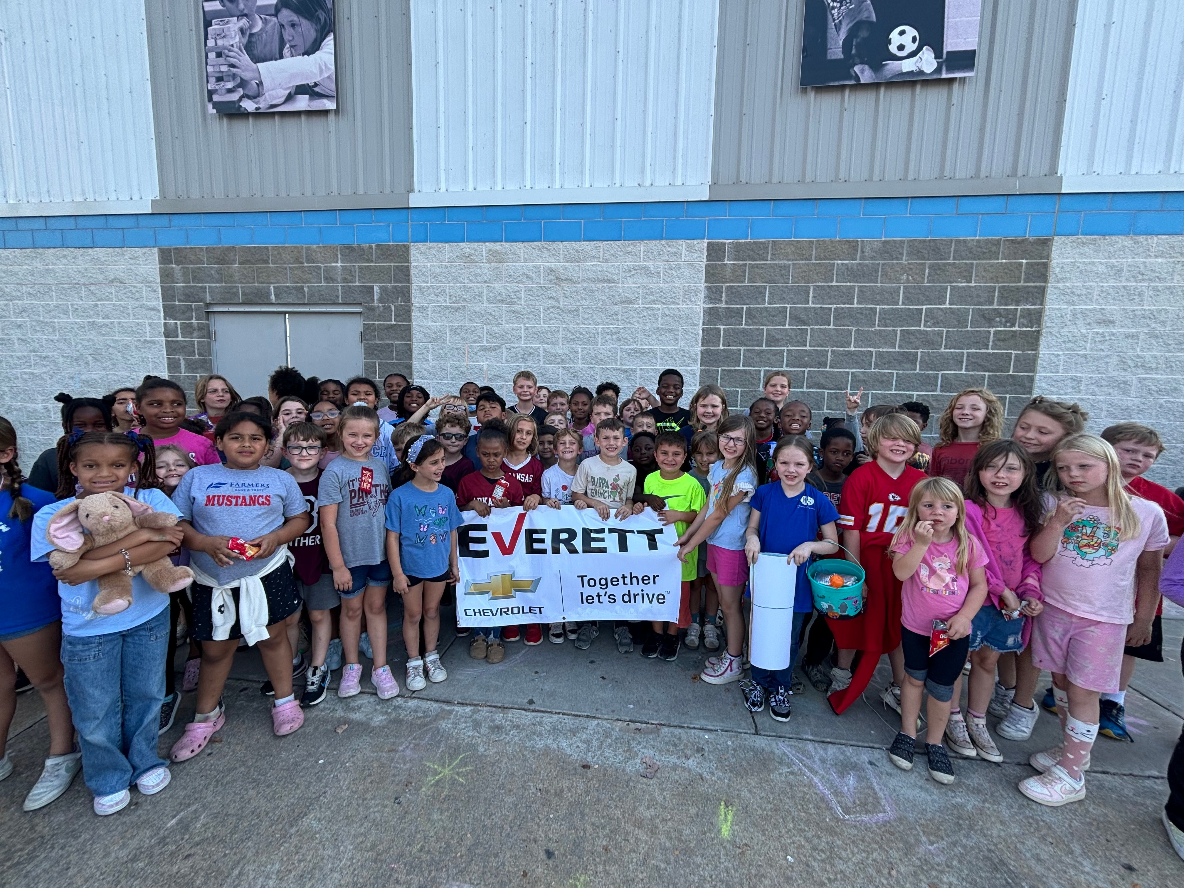 A large group of diverse elementary school children holding an Everett Everett Chevrolet Together Let Drive banner.