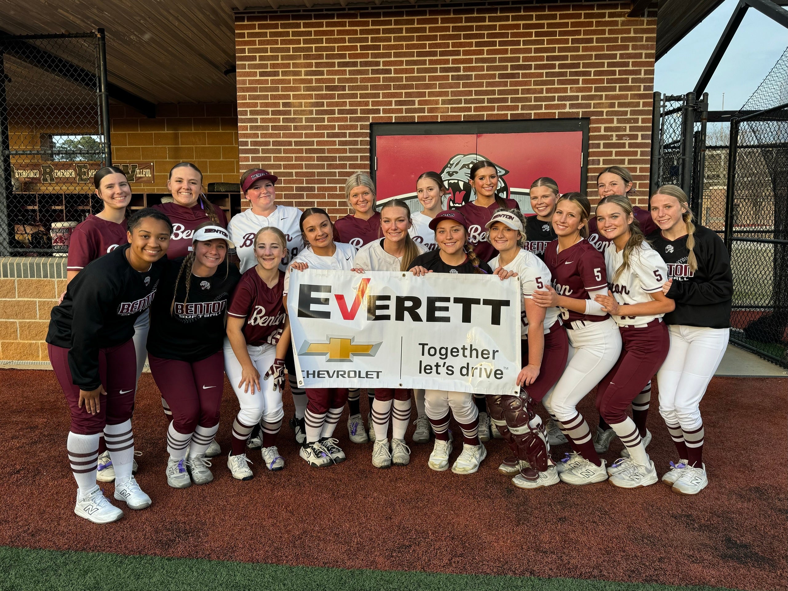 A smiling softball team in maroon and white uniforms holds a white banner for Everett Chevrolet, Together let's drive.