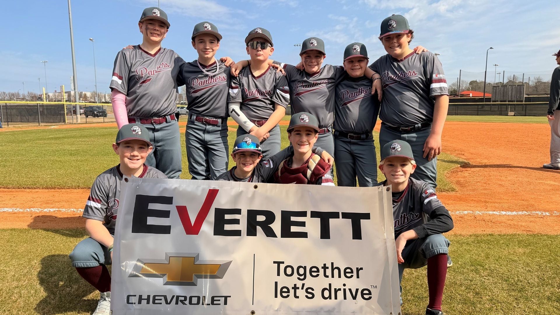 Nine young baseball players in gray uniforms proudly pose with their Everett Chevrolet sponsor banner on a sunny field.