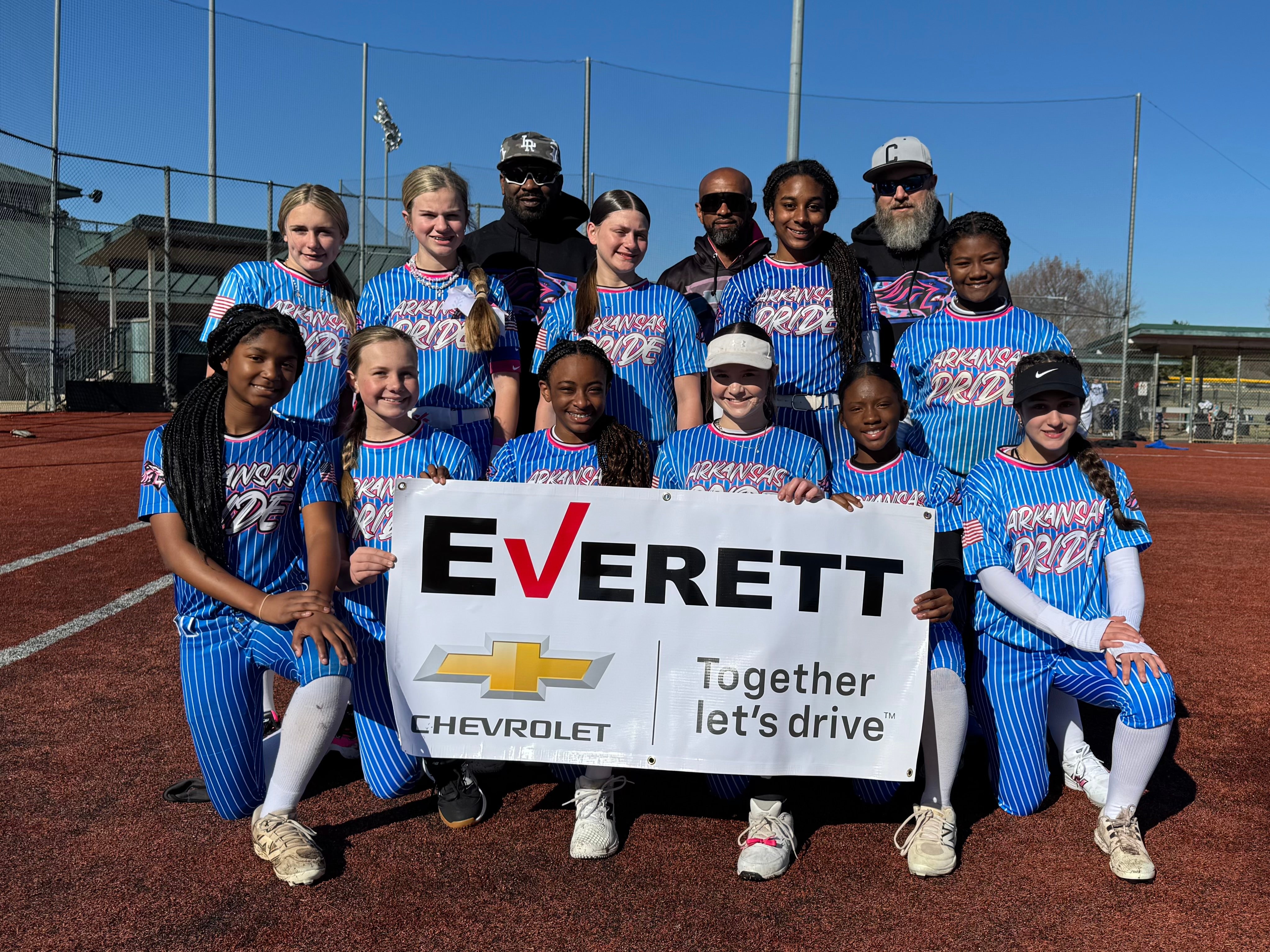Softball team, Arkansas Pride, in blue pinstripe uniforms, with three coaches, holding an Everett Chevrolet banner.