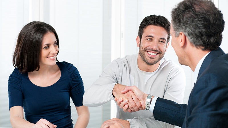 Couple at desk with sales manager, men shaking hands